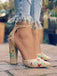 Beige High Heels mit Blumenstickerei, getragen zu zerrissenen Jeans vor verschwommenem Hintergrund im Freien.