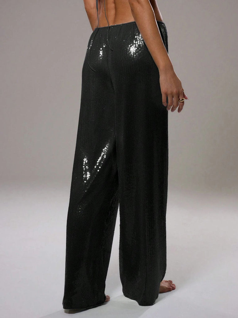Eine Person trägt eine schwarze Paillettenhose vor einem einfarbigen Hintergrund.