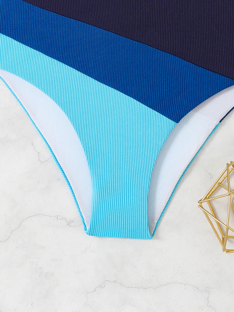 Blau-weißer Badeanzug auf strukturierter Oberfläche mit einem goldenen geometrischen Objekt.