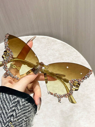 Goldene Sonnenbrille mit dekorativen Elementen, die von einer Hand gehalten wird, vor neutralem Hintergrund