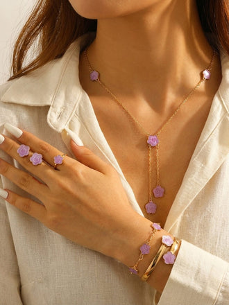 Frau mit lila Halskette, Armband und Ohrringen und einem weißen Oberteil.