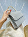 Silberne Clutch, gehalten von einer Hand mit Perlenhenkel, vor einer strukturierten Oberfläche