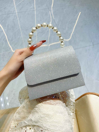 Silberne Clutch mit Perlmuttgriff, von einer Hand gehalten, vor hellblauem Hintergrund