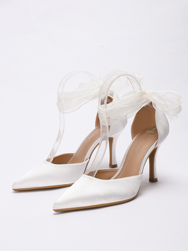 Weiße High Heels mit transparenten Riemchen und Schleife auf weißem Hintergrund