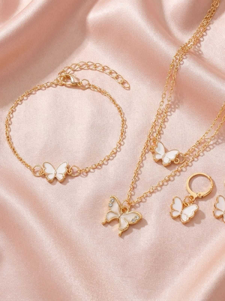 Goldschmuckset mit Schmetterlingsanhängern auf rosa Stoffhintergrund