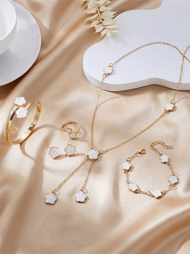 Weißes Schmuckset mit Ringen, Armband und Halskette auf beigefarbenem Stoffhintergrund