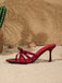 Seitenansicht eines einzelnen bordeauxroten, geknoteten Stiletto-Pantolettes mit Riemchen auf Sand.