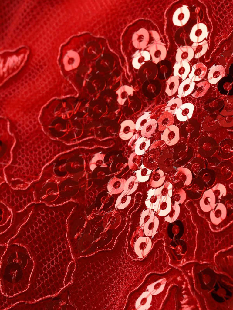 Nahaufnahme des aufwendigen floralen Spitzenmusters auf dem roten Netzstoff, die die feine Handwerkskunst hervorhebt.