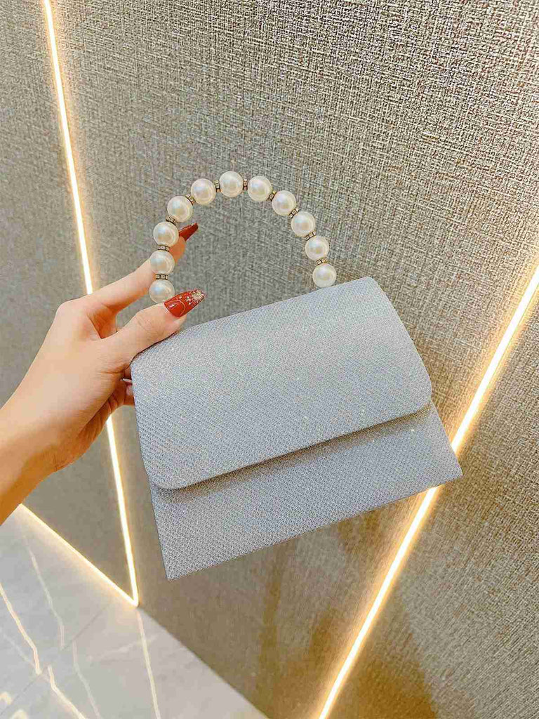 Eine Hand hält eine hellblaue Handtasche mit Perlmuttgriff vor einem neutralen Hintergrund.