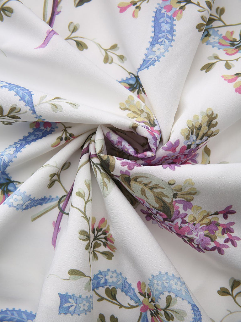 Eine wirbelnde Ansicht des weißen Stoffes, die die weiche Textur und den lebendigen botanischen Druck zur Geltung bringt.